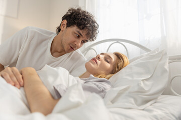 Man gently talking to women lying in bed with closed eyes, symbolizing emotional connection, care, relationship healing, support, intimacy and quiet moment between couple at home.