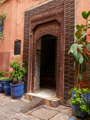 Ornate Wooden Doorway with Traditional Carvings and Studs Leading to a Tiled Moroccan Interior, Flanked by Potted Plants in Marrakech