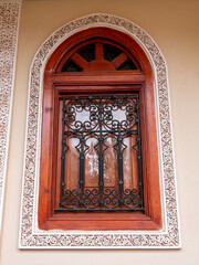 Ornate Arched Wooden Window with Wrought Iron Grille and Intricate Plaster Carvings on a Traditional Moroccan Building in Marrakech
