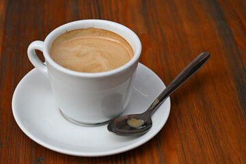 Close-up of a coffee cup with a spoon on a wooden café table.