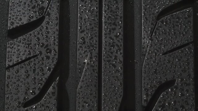 Wet Surface of a Car Tire Close Up. The surface of a car tire covered with shiny water drops slowly floats in front of the camera close-up