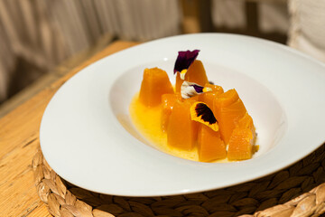 Designer melon dish with edible flowers on wooden table in sunlight under palm shadow