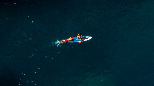 Aerial close-up of a couple swimming in the sea with a stand-up paddleboard. Sup concept. - Powered by Adobe