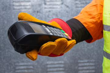 Construction worker wearing protective gloves and reflective workwear holding a wireless payment terminal. Concept of digital transactions, contactless payments in the construction industry.
