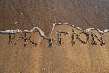 The word “Vacation” written on the sand by the sea
