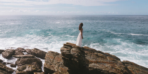 Aerial drone view of bride in an amazing dress standing on a cliff and looking