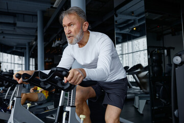 Elderly man riding an exercise bike in a bustling gym