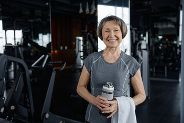 Senior woman displaying a happy smile holding a bottle of water in a gym