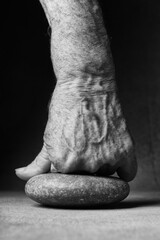 An elderly man's fist rests on a stone. Conceptual photography. Concept of resilience, strength of character, overcoming difficulties, illnesses and life's troubles. Toned image, black and white