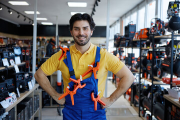 A man in overalls holds clamps on his shoulder in a store