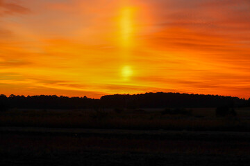 A sensational sunset or sunrise floods the sky with vibrant shades of orange and yellow, featuring a dramatic light pillar at the center.