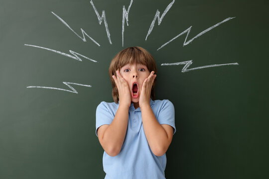 Back to school. Emotional boy near chalkboard with drawn lightning bolts indoors