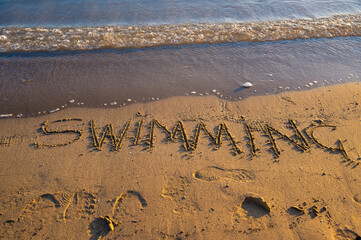 The word “Swimming” written on sandy beach near the shoreline
