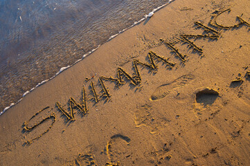 The word “Swimming” written on sandy beach near the shoreline