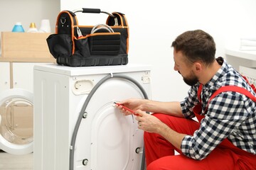 Professional repairman fixing broken washing machine indoors