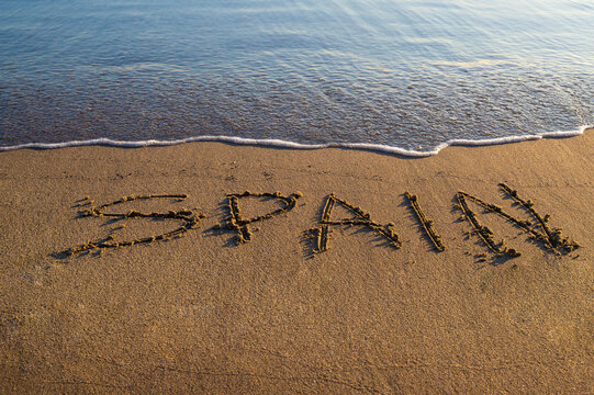 The word “Spain” written on sandy beach near the shoreline