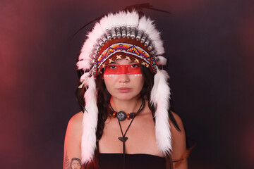 Shaman woman in native American Indian headdress with face painting on dark background with smoke