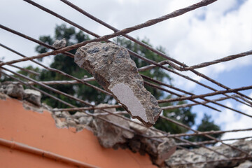 Close-up of exposed steel rebar with a chunk of concrete after roof demolition, set against the sky and trees, in an Indian building under renovation.