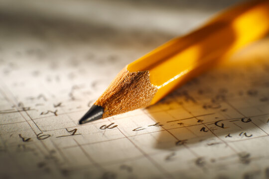 Macro shot of a sharpened yellow pencil placed on paper filled with handwritten mathematical equations and symbols in soft natural lighting