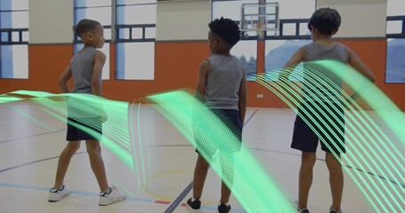 Standing three boys in athletic wear facing basketball hoop on court, with green ribbon graphic