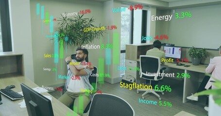Stretching Indian man wearing striped shirt leaning in open office with floating finance metrics