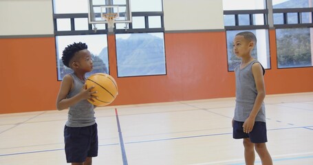 Two boys wearing matching gray uniforms playing basketball in gym court, with hoop and court lines