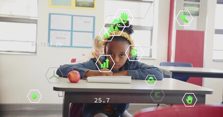 Child wearing yellow headband and denim jacket writing in classroom, with notebook pencil red apple
