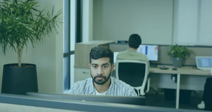 Working man wearing striped shirt sitting at desk in open-plan office, with desktop monitor