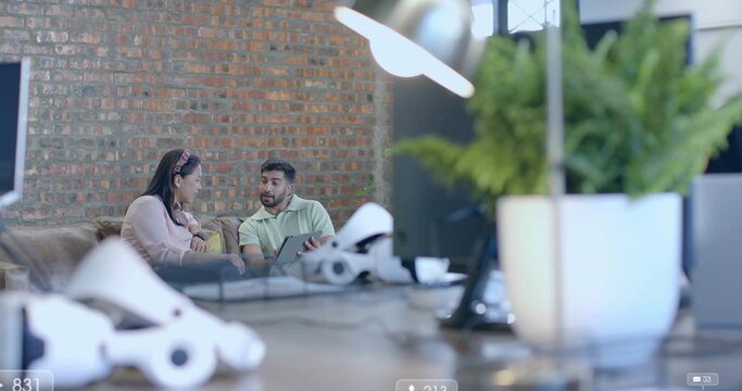 Indian man in polo and woman in sweater reviewing tablet in office lounge, with VR headsets