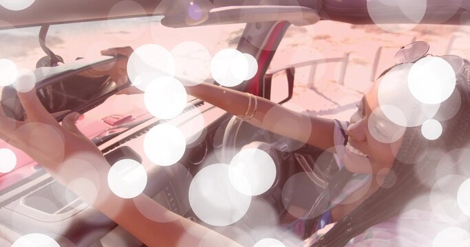 Reaching up woman wearing tank top adjusting rearview mirror in car by sandy roadside, copy space