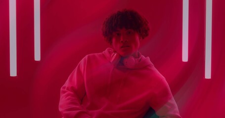 Sitting man wearing hoodie and over-ear headphones on chair in red studio, with vertical neon tubes