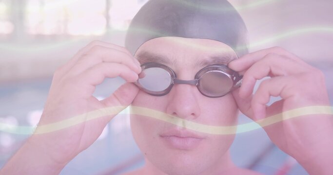 Adjusting dark goggles, swimmer wearing black swim cap standing at lap pool edge, with pastel haze