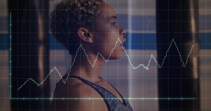 Female athlete in athletic top holding boxing stance in gym, with punching bags, graph overlay