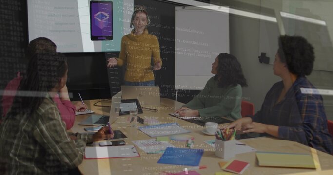 Presenting woman in mustard top pointing at app display in meeting room, with laptops, notebooks - Powered by Adobe