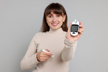 Diabetes test. Woman with lancet pen and glucometer on light grey background, selective focus