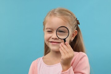 Little girl with magnifying glass on light blue background