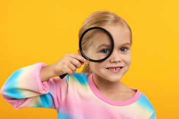 Little girl with magnifying glass on yellow background