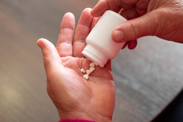 An elderly woman pouring heart-shaped pills from a bottle. Hands pouring white heart-shaped tablets from a small white bottle into the palm, care for the heart and the fragility of health in old age