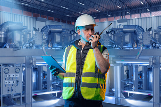 Industrial engineer oversees machinery operation, using radio communication and tablet for monitoring, coordination, and safety control in a modern factory.