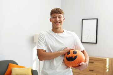 Halloween celebration. Man holding pumpkin with drawn spooky face indoors