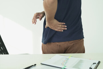 An asian businessman overworks and feels pain in his back from using a laptop, hand holding and rubbing hurt area, numbness in the waist area and back and a kind of health care and medical concept.	
