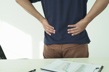 An asian businessman overworks and feels pain in his back from using a laptop, hand holding and rubbing hurt area, numbness in the waist area and back and a kind of health care and medical concept.	
