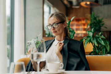 Portrait of a beautiful business woman sitting in a bright restaurant using a mobile phone.