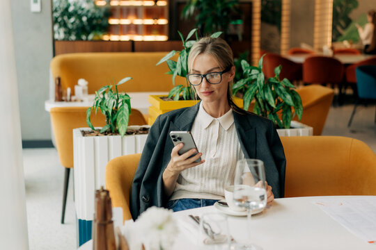 Blond middle-aged caucasian business woman in restaurant using mobile phone.