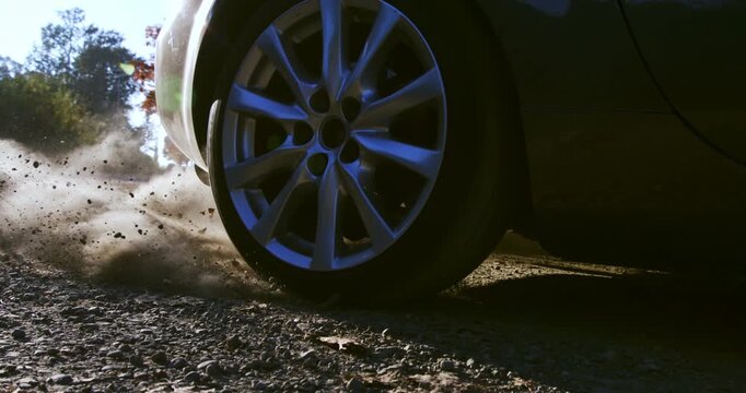 Slow motion close up of car wheel accelerating on gravel terrain, lifting dust and debris at 1000 fps.. Perfect for concepts of adventure, energy, and motion.