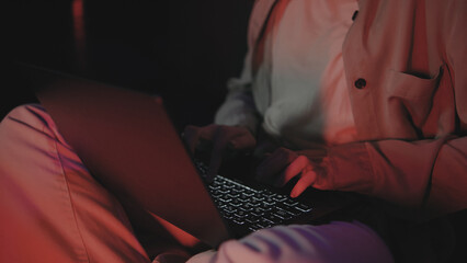 Working late at night on a laptop in a dimly lit room with warm red and orange lighting creating a cozy atmosphere © tol_u4f