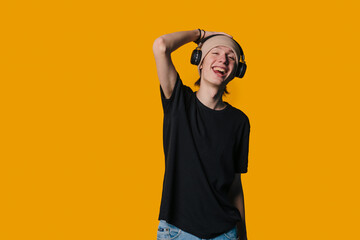 young guy with headphones smiling, male youth with headphones on orange background smiling broadly