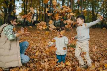 young children excitedly leap and scatter crispy autumn foliage amidst sundappled woodland scene