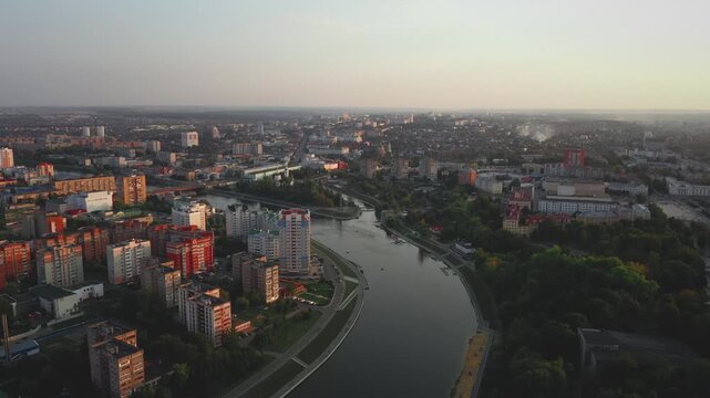 Aerial evening view of Orel city in Russia with river, Strelka, main buildings, churches and roads. Beautiful cityscape with lights reflecting on water at sunset, showing urban architecture, skyline.