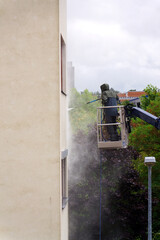 Unrecognizable man cleaning facade surface from lifting platform with high pressure stream of water